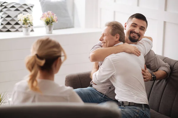 dois homens gays se abraçando e sorrindo enquanto a psicóloga de costas, observa a cena.